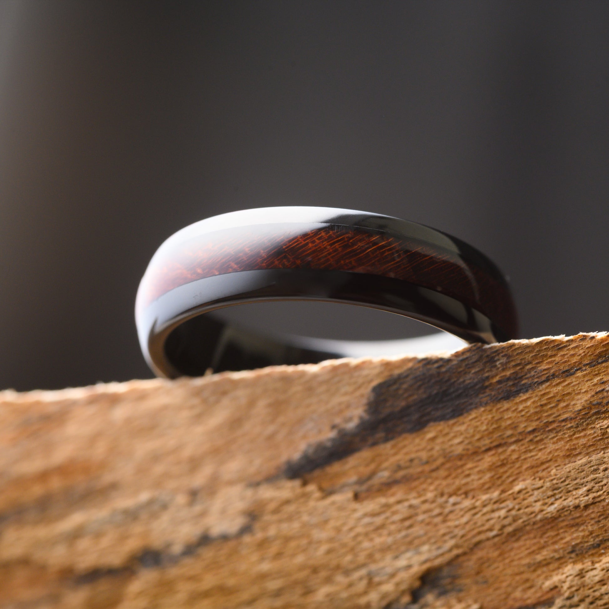 black and rosewood tungsten ring resting over the edge of a textured shelf