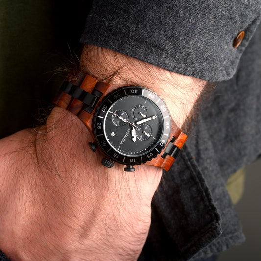 Wooden watch with black face on a wrist against a dark background