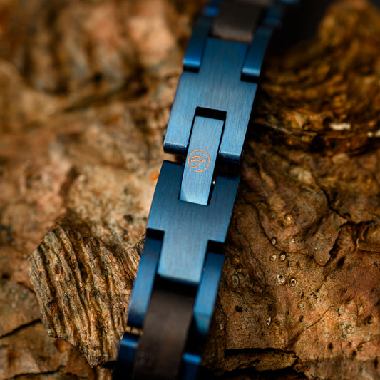 A close up shot of the blue steel bracelet link showing the botanica logo resting on a backdrop of drift wood