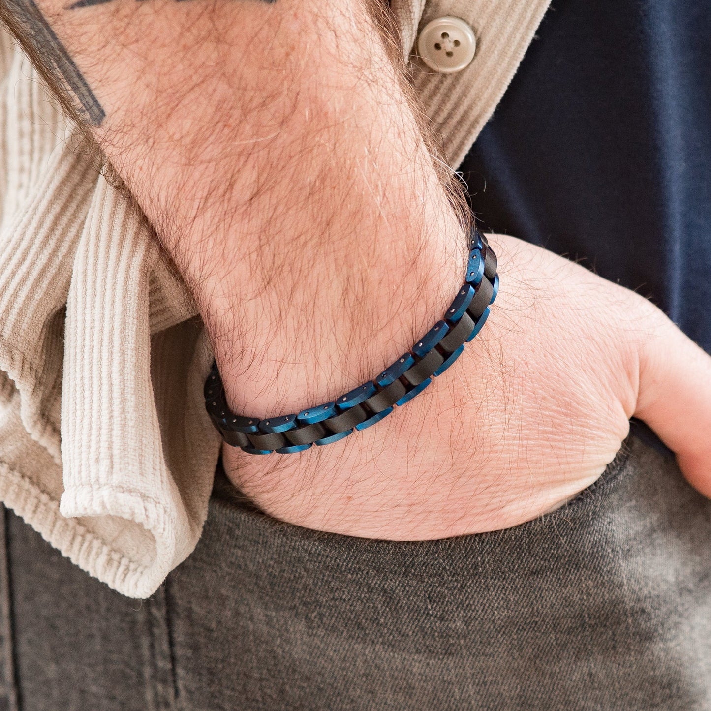 A shot of a man wearing a blue steel and sandalwood bracelet with hand in pocket