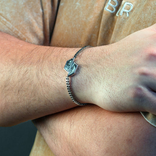Close-up of a wrist wearing a silver bracelet with a hexagonal charm.