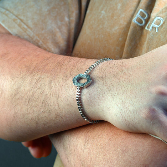 Silver hexagonal bracelet on a person's wrist with a blurred background
