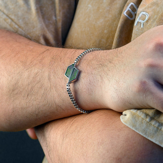 Close-up of a wrist wearing a silver bracelet with a green gemstone.