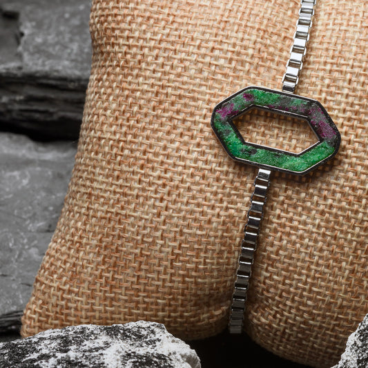 Hexagonal green stone pendant on a chain against a textured beige background