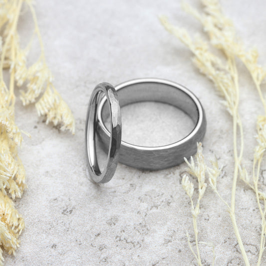 Two silver rings on a textured surface with dried plants around