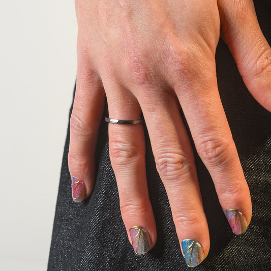 Close-up of a hand wearing a silver ring with metallic nail polish on a neutral background