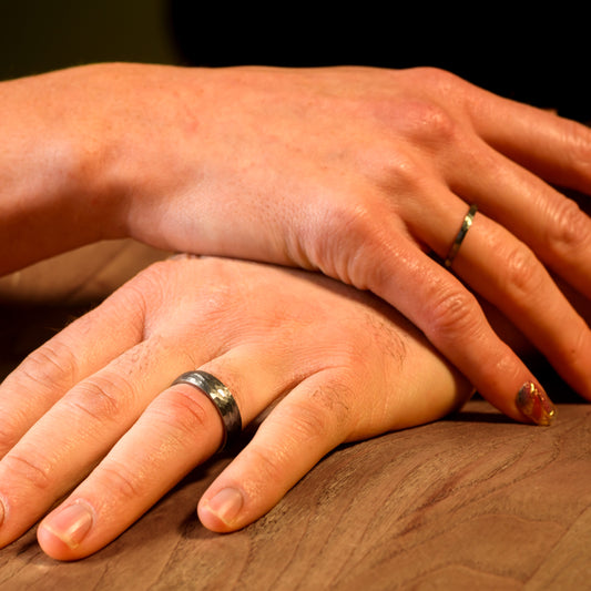 Two hands with silver wedding rings on a wooden surface