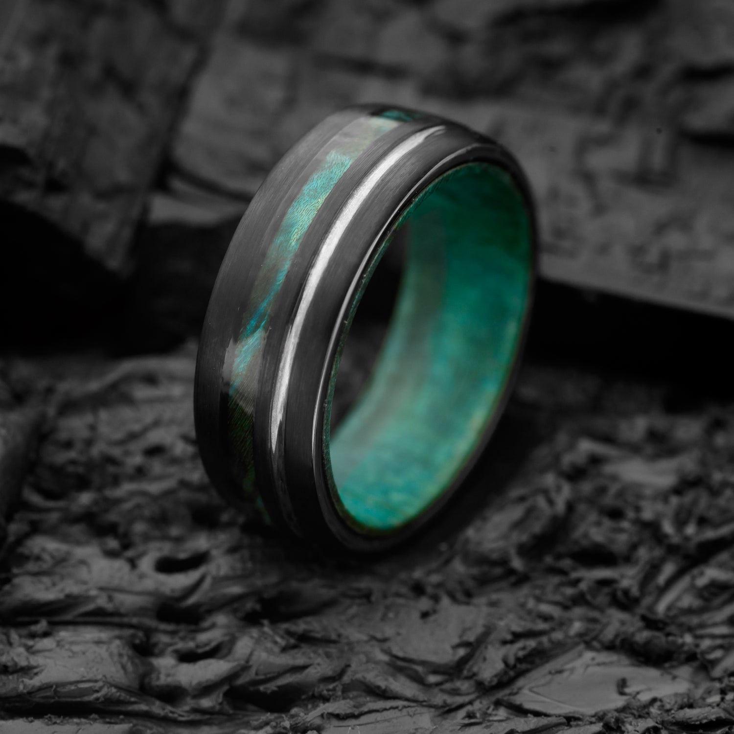 A Tungsten Steel Ring with 8mm width, dual inlay of blue canadian maplewood and silver resting on a bed of charcoal
