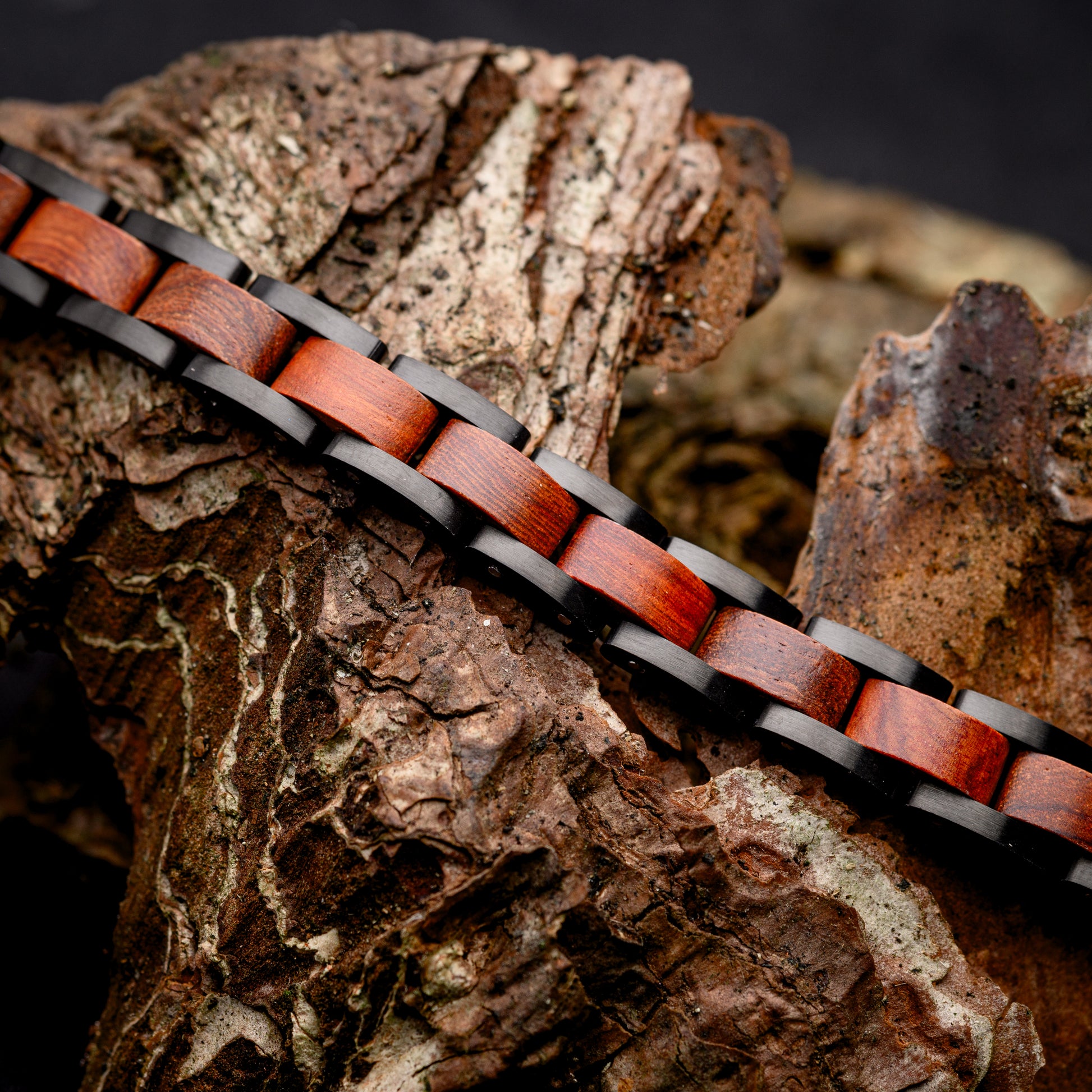 A Mens Tungsten Steel Bracelet with rosewood internal links resting across a driftwood piece