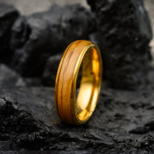 gold tungsten ring with walnut wood inlay resting on a stone background for men or women