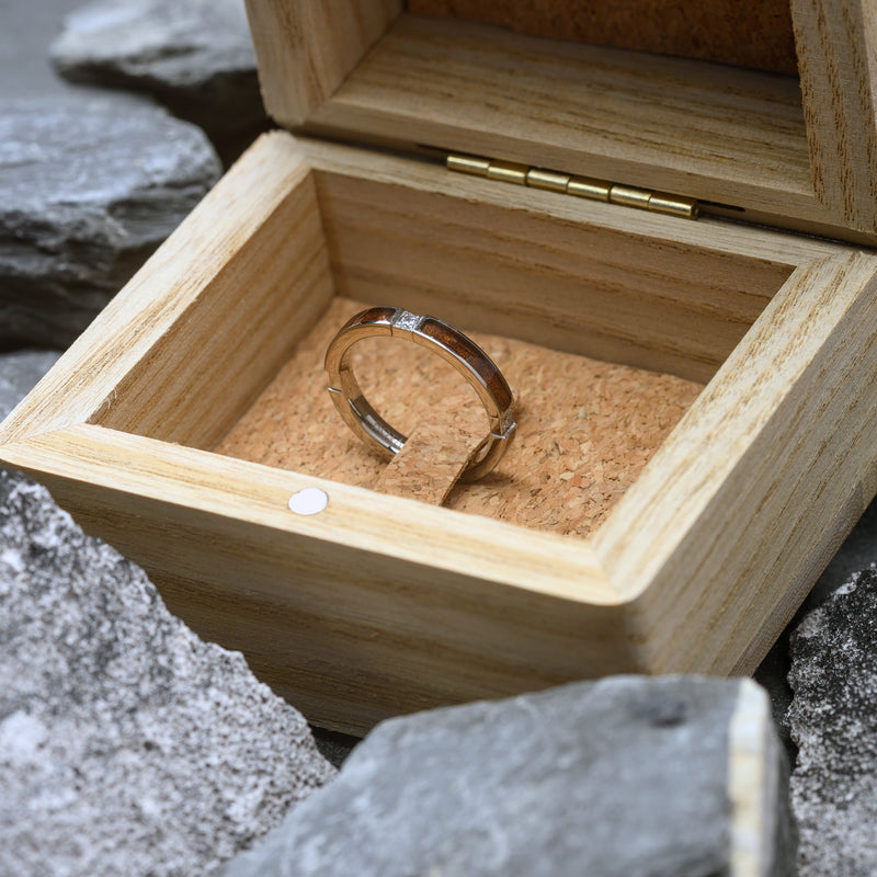 Wooden jewelry box with a Silver ring inside, placed on a rocky surface.