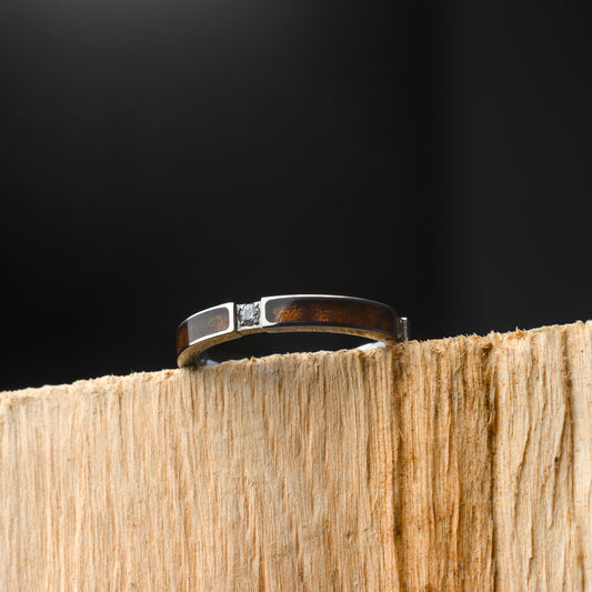 Silver ring with a diamond on a wooden block against a black background
