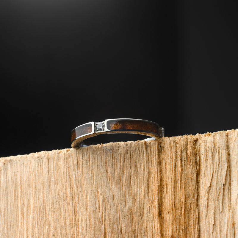 Silver ring with a diamond on a wooden block against a black background