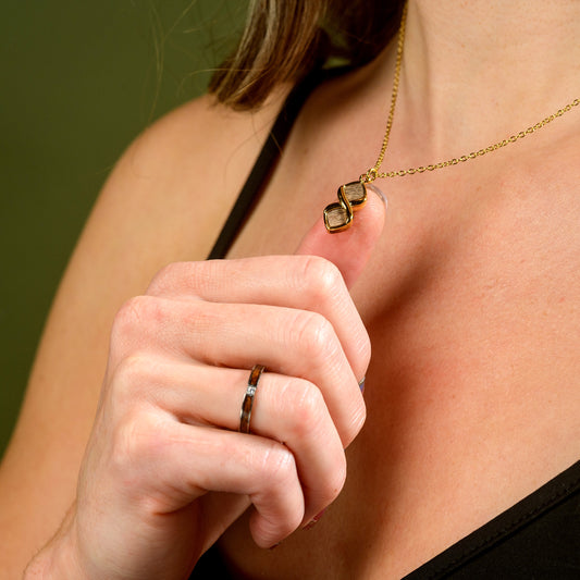 Close-up of a person wearing a gold necklace with walnut wood, holding their hand near their neck.