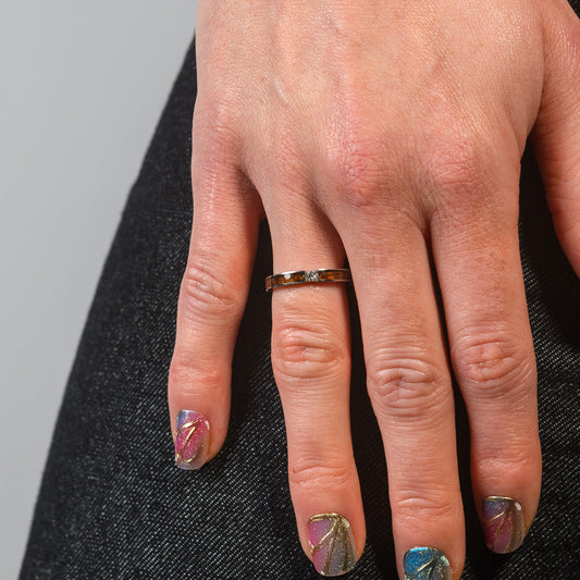 Hand with decorative nails and a gold ring on a gray background