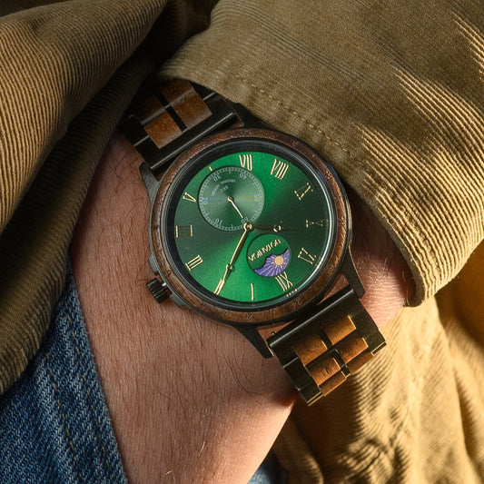 Wooden wrist-watch with a green face on a wrist, against a brown fabric background