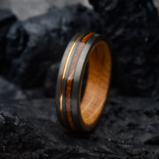 tungsten steel ring resting on a stone backdrop with whiskey wood inlay and rosegold band for men or women