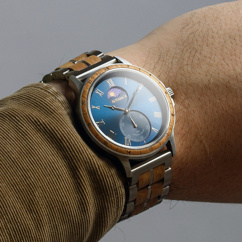 Wrist wearing a watch with a blue face and wooden strap on a neutral background