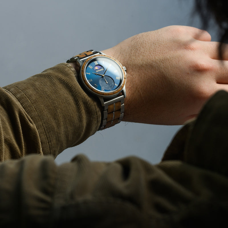 Close-up of a wrist wearing a watch with a detailed face, against a neutral background.