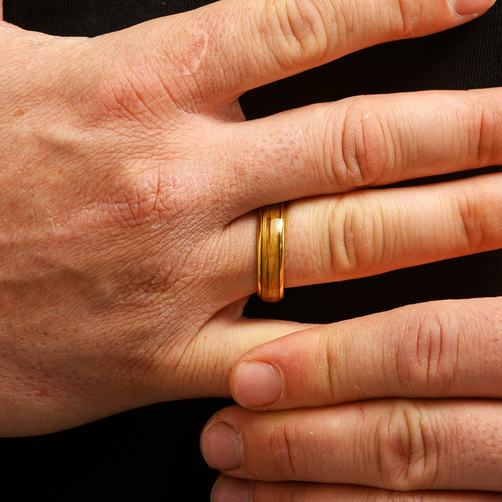 close up hand wearing gold tungsten ring with walnut wood inlay
