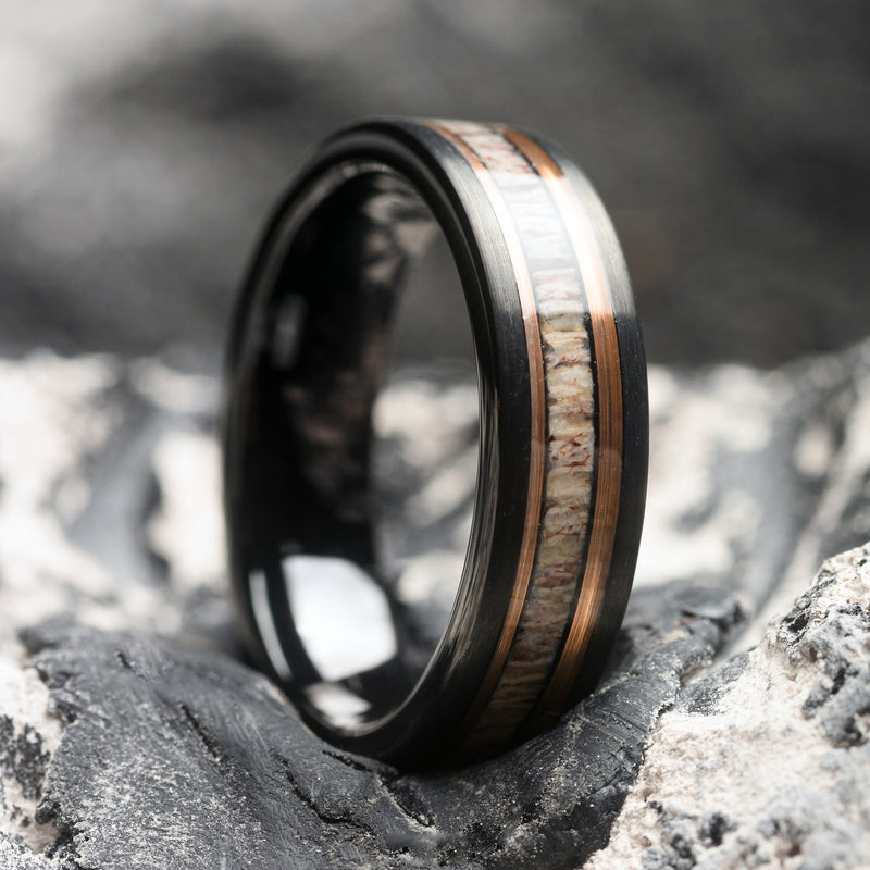 Tungsten ring with Deer Antler Inlay and a Rosegold band, on a textured stone surface