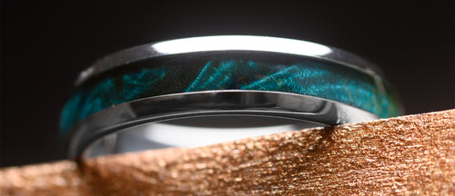 Close-up of a silver ring with blue maplewood inlay on a wooden surface