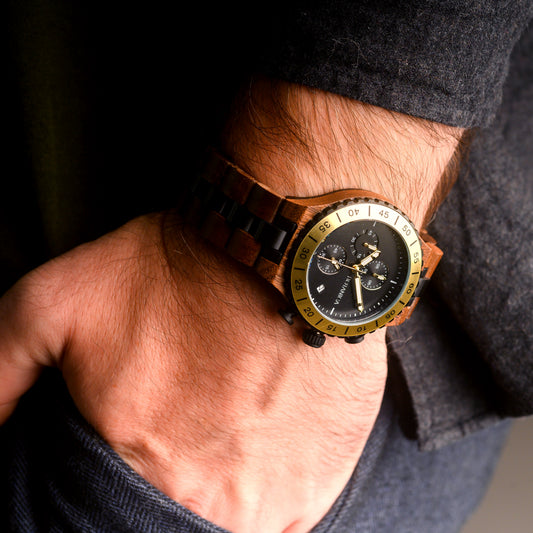 Wooden wristwatch with a detailed face and gold accents on a person's wrist.