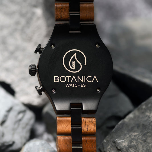 Back of a Watch with wooden strap and black case on a rocky background, featuring Botanica Watches logo.