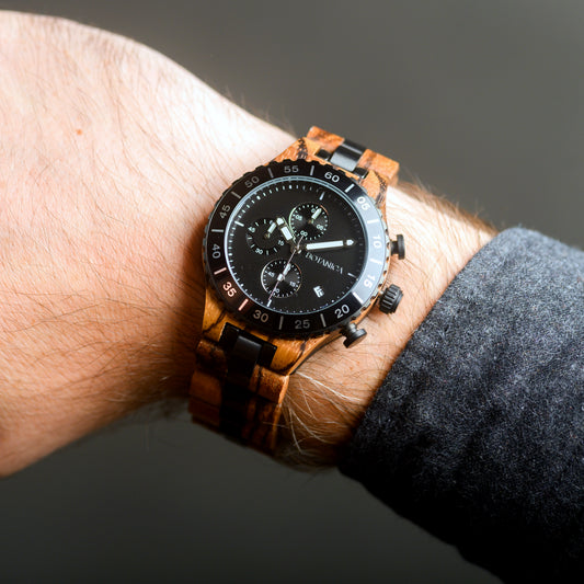 Wooden wristwatch with black dial on a wrist against a dark background